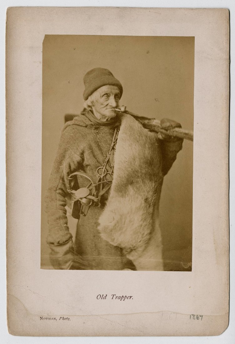 WILLIAM NOTMAN, "OLD TRAPPER”: WILLIAM NOTMAN, "OLD TRAPPER”. This is an early portrait by Notman of a Canadian trapper. He has his trap slung over his shoulder and a pelt is suspended from a board. 5 ¼ x 3 3//8- inch albumen pr