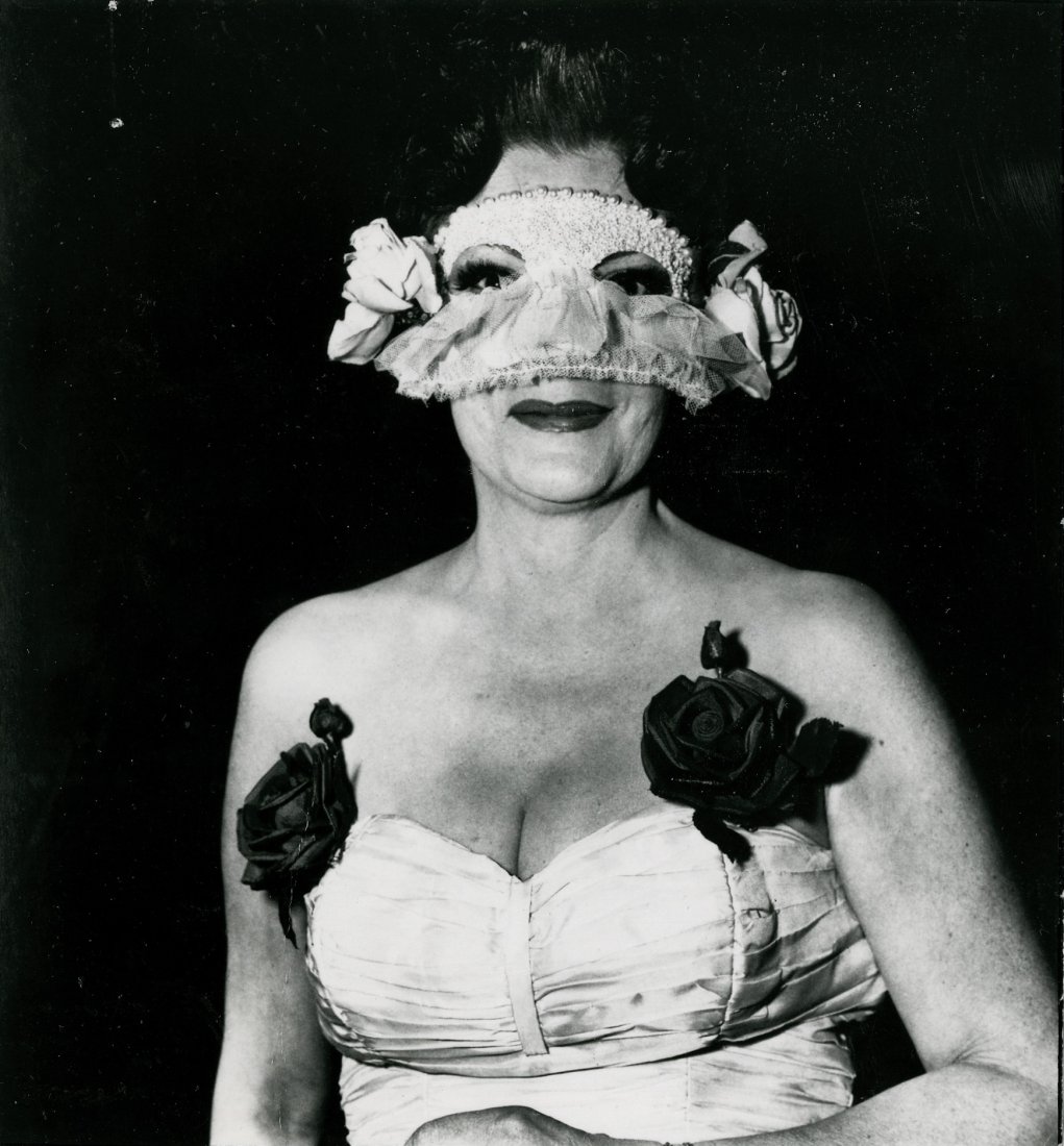 DIANE ARBUS, "LADY AT A MASKED BALL WITH TWO ROSES IN: DIANE ARBUS, "LADY AT A MASKED BALL WITH TWO ROSES IN HER DRESS, NYC. 1967". 4 5/8 x 4 3/8- inch ferrotyped gelatin silver print with an "Aug 7, 1977" date stamp on verso. Also, in red pen, "Text Dolo