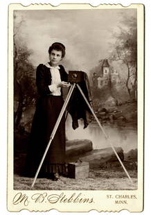 A woman photographer with her camera.: A woman photographer with her camera. She is M. B. Stebbins, St. Charles, Minn., or the wife who has taken over the business. There’s a plate holder on the ground, and a romantic European landscape