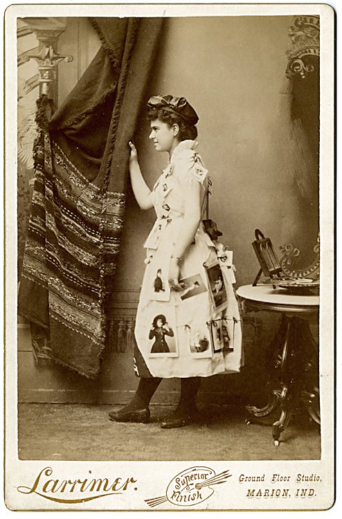 A photo advertising lady, posed in profile, with: A photo advertising lady, posed in profile, with cabinet cards attached to her dress. A frame is on the table behind her. By Larrimer, Marion, Indiana.
