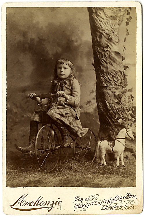 A girl on a tricycle with a toy stuffed horse.: A girl on a tricycle with a toy stuffed horse. By Mackenzie, Dubuque, Iowa