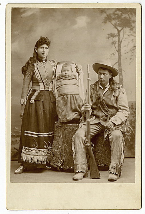 An Indian family.: An Indian family. They wear Indian dress and the man has a rifle, and the baby is in a papoose cradle with a decorated collar around its neck. They are nevertheless presented as a typical family, with