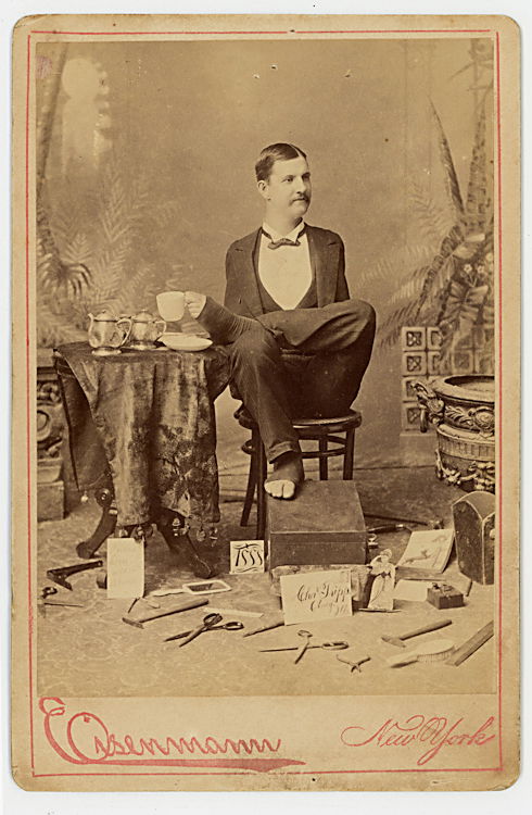 Charles B. Tripp, armless wonder.: Charles B. Tripp, armless wonder. He uses his feet to perform complex tasks. In this cabinet card by Eisenmann he lifts a cup from the table. On the floor are scissors and other tools and examples of
