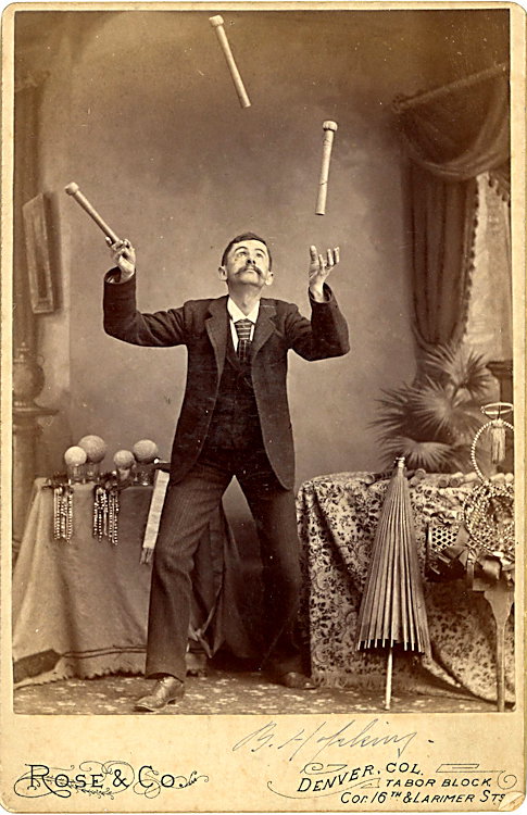 A juggler with sticks up in the air.: A juggler with sticks up in the air. There are balls in glasses on the table to the left. A strange prop is on the extreme right. Cabinet card by Rose & Co., Denver, Colorado. Possible signature on th