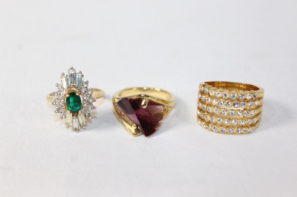 Costume Jewelry Lot of 3 Rings: 2 18K Gold Plated Rings one marked HGE. Purple, Green and clear, and clear rhinestones, as pictured.