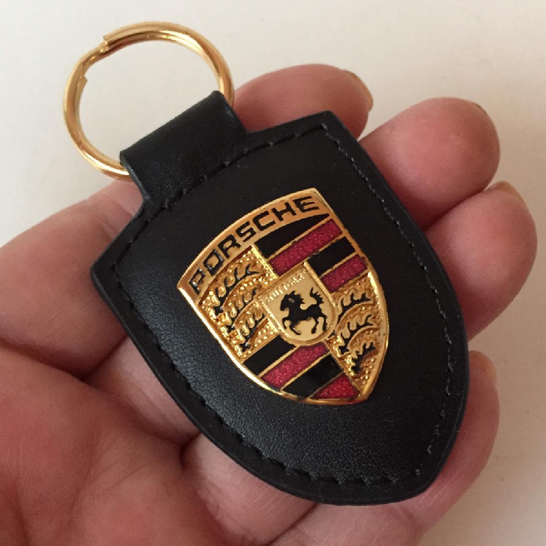 Black leather PORSCHE gold plated symbol with: Black leather PORSCHE gold plated symbol with multicolor enamel keychain. Length 3". Condition excellent.