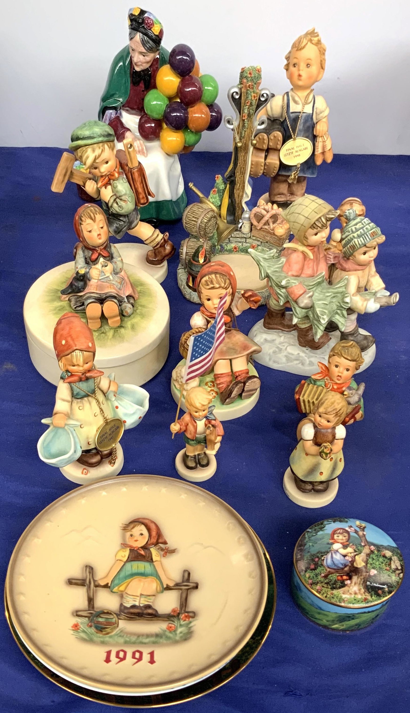 Lot of Hummel Figurines, Plates, etc.: Also, a Royal Doulton Figurine, "The Old Balloon Seller", and a 1993 Weihnachten Plate. The Hummel Items include: a 1991 Hummel Plate, a Danbury Mint Hummel "Maypole" Plate, a Danbury Mint "Apple Tree