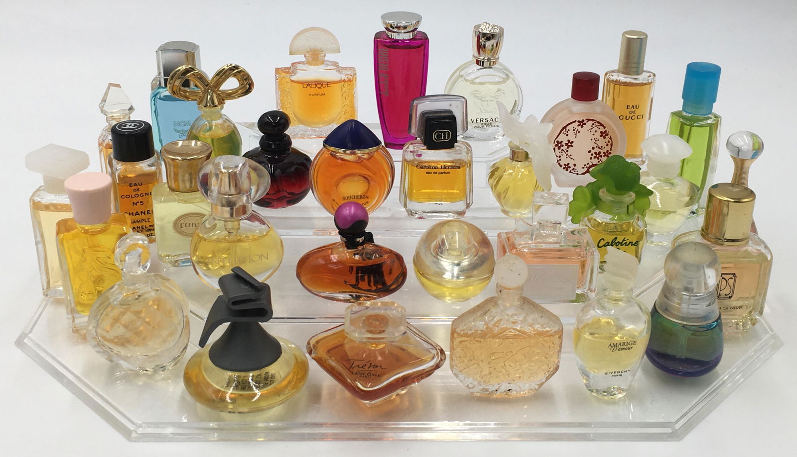 Lot of 31 Miniature Perfumes, Most are Nearly Full: Includes: Dior, Versace, Gucci, Chanel and Lalique. The Stand is Included. The Tallest Perfume Measures 2 3/4" in Height. Third-Party Shipping or Personal Pickup Required.