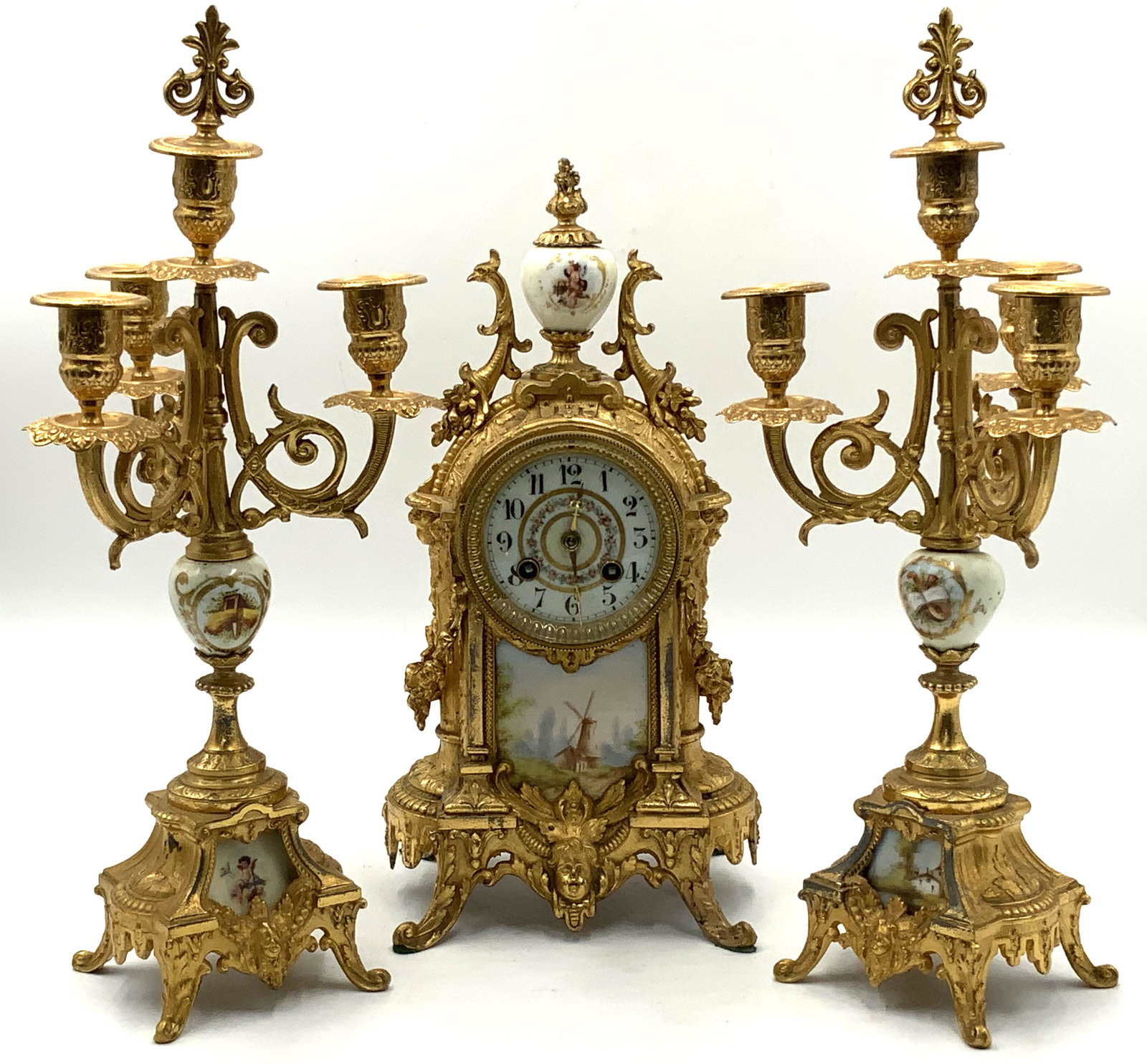 French-Style Old Porcelain & Metal Clock Set.: Mostly Hand-Painted. The Clock Works are signed P. Mente et Cie. With Key & Pendulum. The Clock Measures 14" Tall. The Candleholders Measure 16 1/4" Tall. Working Condition on the Clock is Not Known. 