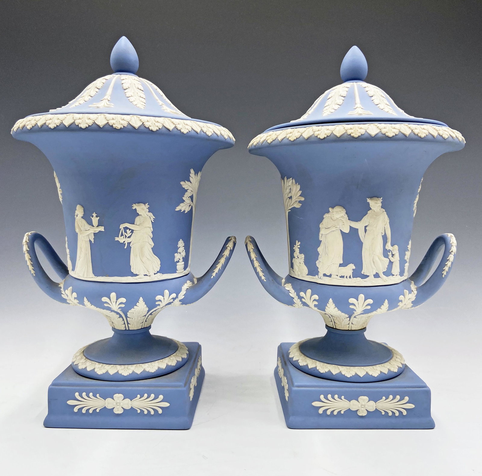 Pair of Wedgwood Jasperware Campagna Covered Urns.: These are marked "Made in England". They are Powder blue, with white designs. Each measures 12" tall, including the lid. They are Moderately heavy, in Nice condition, with a few areas of mild discolor