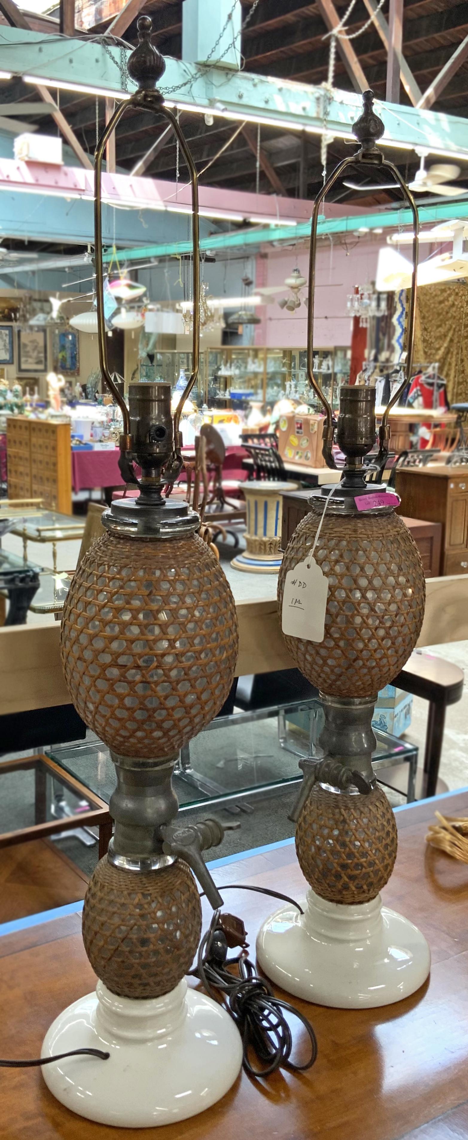 Pair of European Liquid Dispenser Lamps.: This pair of lamps has woven wicker covers over glass globes with pewter nozzles, sitting on porcelain bases. They measure 29" tall to the top of the harp. The base measures 6 1/2" across. Third Party