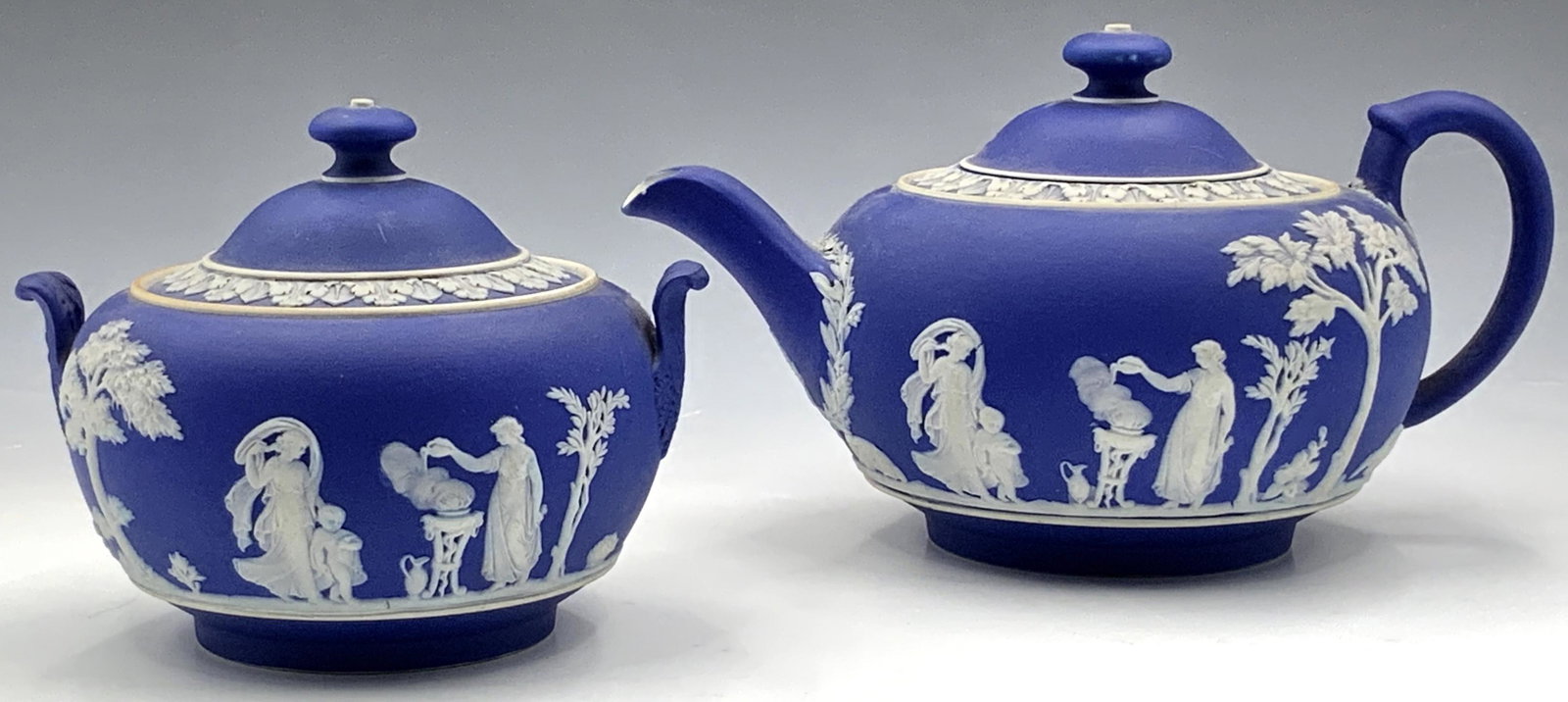 Lot: Wedgwood Jasperware Teapot & Sugar Bowl.: As Is. These are both 19th Century pieces. Both are cobalt blue, with Grecian-style white relief images. The undersides of both pieces read, "Wedgwood" in all capital letters. Both pieces have hairlin