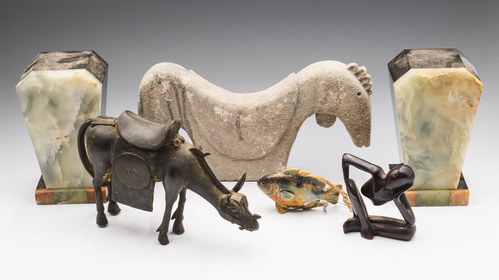 Lot: 4 Sculptures, One Pair of Onyx Bookends.: The sculptures include a stone horse, a white metal horse, a light stone nude figure, and a hanging fish ornament. The bookends have a few Chips. The largest piece measures 12" long. Third-Party Shipp