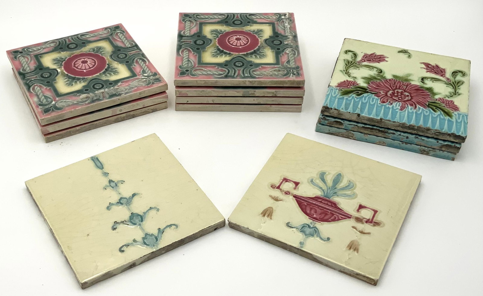 Lot of 11 Art Nouveau Majolica 6" Tiles.: 7 of the tiles are matching, with a central pink medallion surrounded by a green border. 3 of the other tiles are of a different matching design, with red flowers and a yellow background. These tiles 