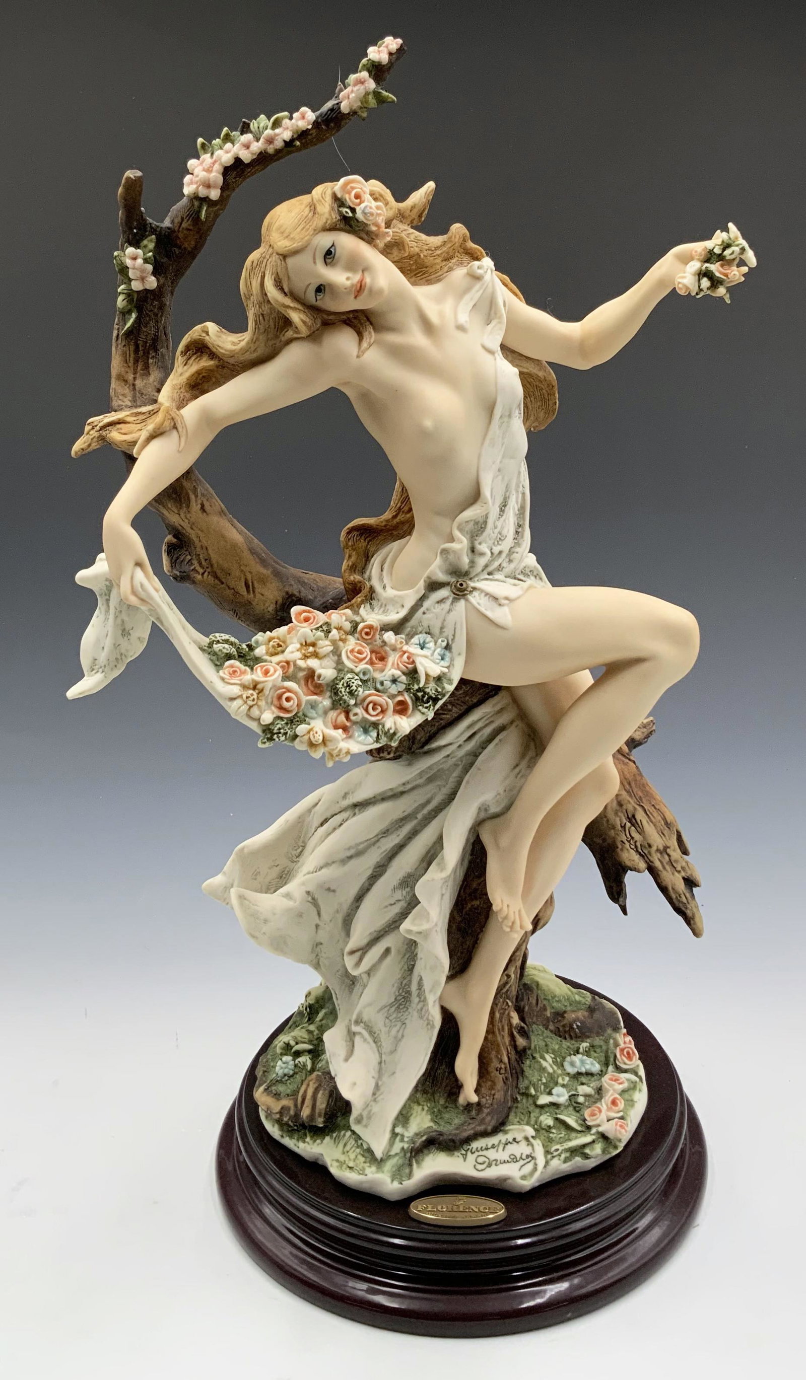 Giuseppe Armani Figurine of Woman in a Tree.: A Florence figure. The Figurine is a partially nude maiden with flowers, Signed by the artist. It appears that the top of the branch is Chipped. The Figurine measures 16 1/2" tall and 9" wide. Third-P