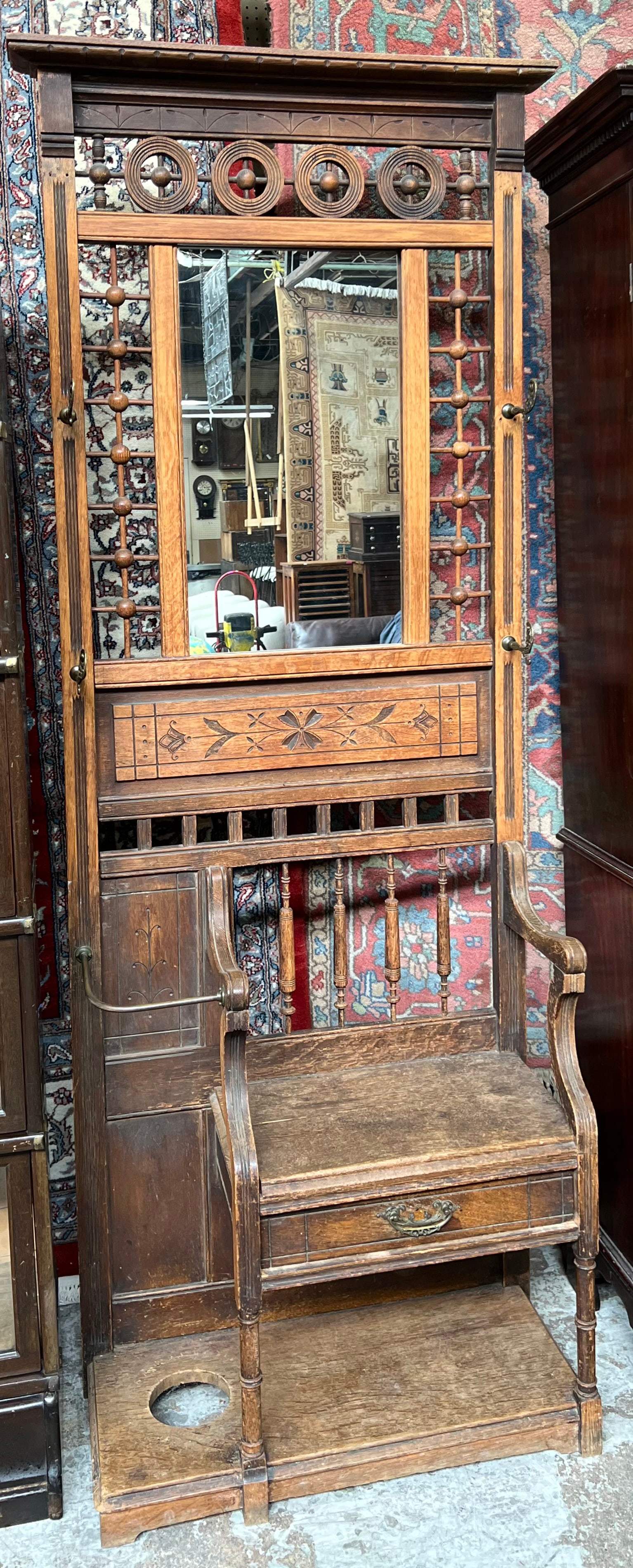Victorian Stick & Ball Oak Hall Tree w/ Bench.: The Hall tree has a mirror, ornate metal coat hooks, an umbrella stand with a drip pan, and a bench with one Drawer. The piece has several scratches and dings, commensurate with age. It measures 30" w