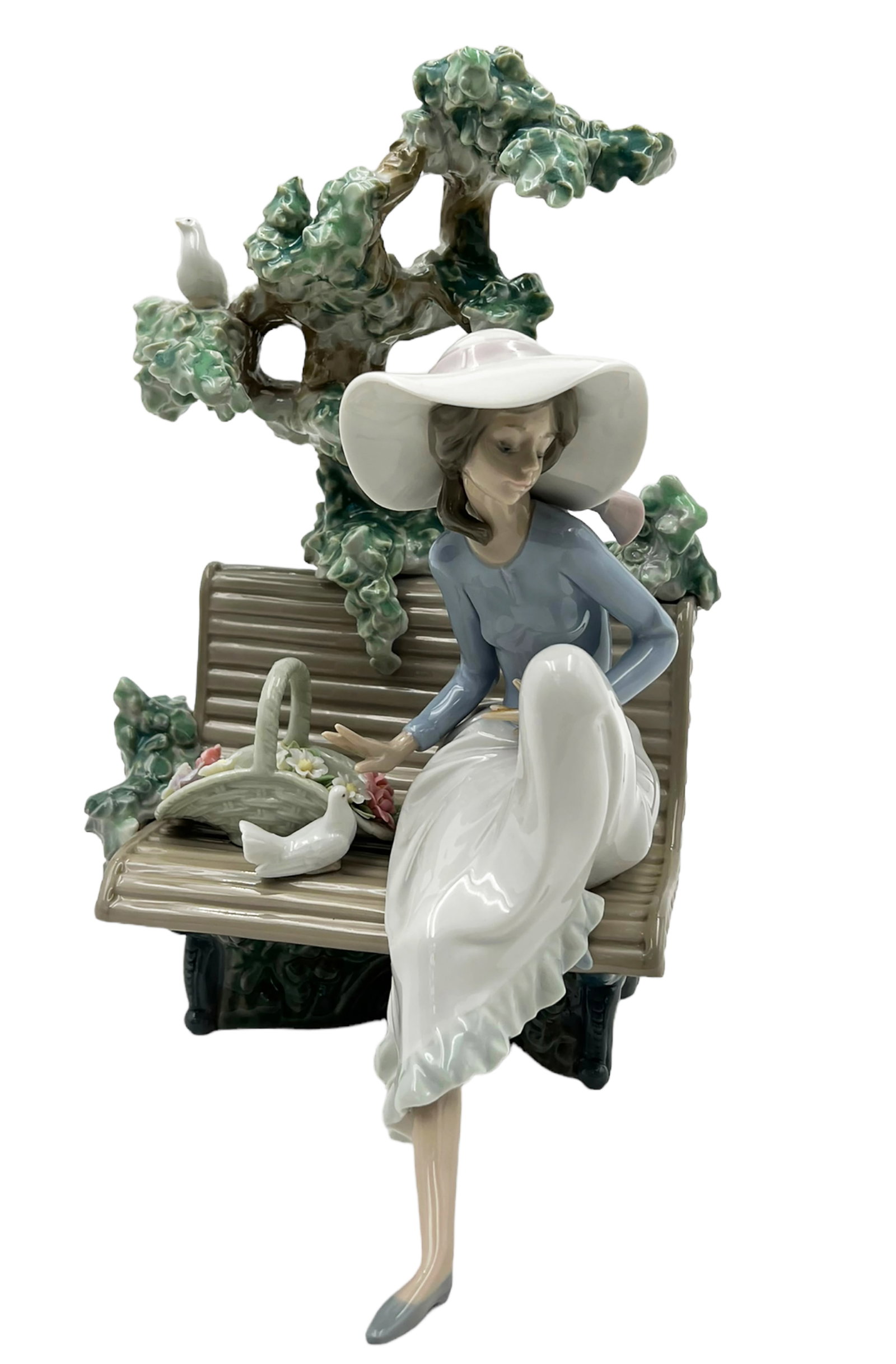 Lladro "Sunday in the Park" Figurine.: The figure is of a young woman in a hat, seated on a bench. There is a tree growing behind her, and a basket of flowers next to her. Two white doves are her companions. The figure looks to be in Nice 