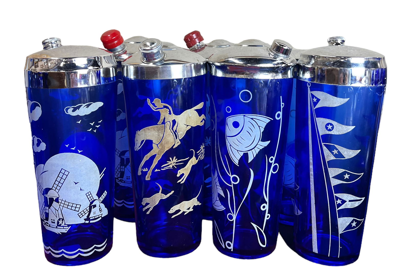 Lot of 7 Mid Century Blue Glass Cocktail Shakers.: They may be Hazel Atlas. Two have a fish design, two have a windmill design, two have a fox hunt design, and one has a flag design. There is some minor surface wear; overall, the lot looks to be in Go