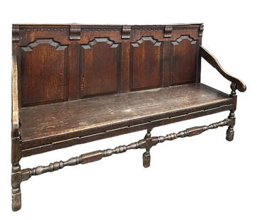 Primitive Oak Bench.: This large oak bench has a back with beautiful fielded panels, curved arms on both sides, and stretcher legs. The top of the bench features intricate carved decorations. The apron of the bench has a r