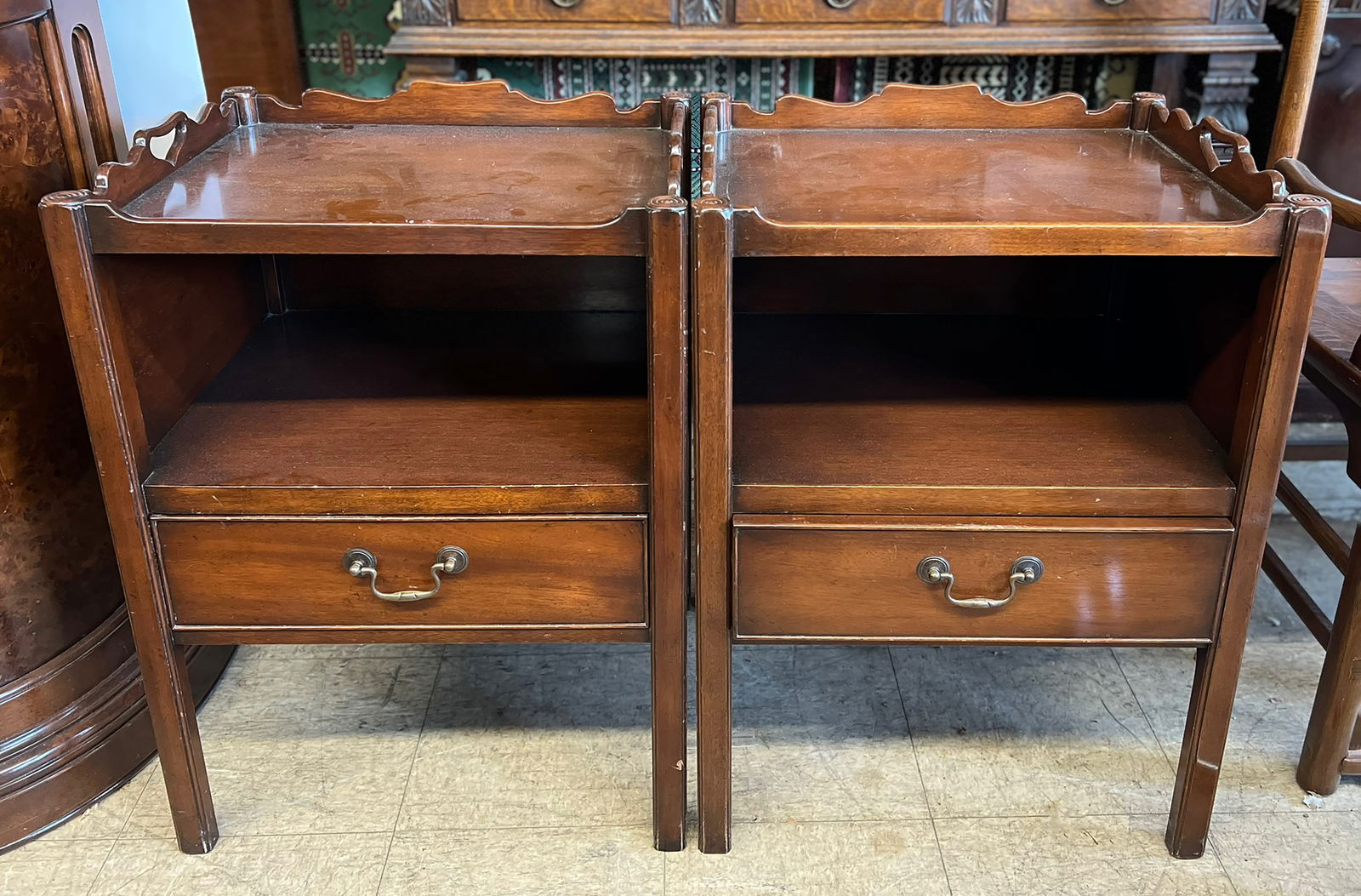 Pair of Mahogany End Tables.: This is a pair of mahogany end or lamp tables with tray tops. The tables each have carved side handles on the top and lower shelves. Both tables have a lower drawer with brass handles. They are in use