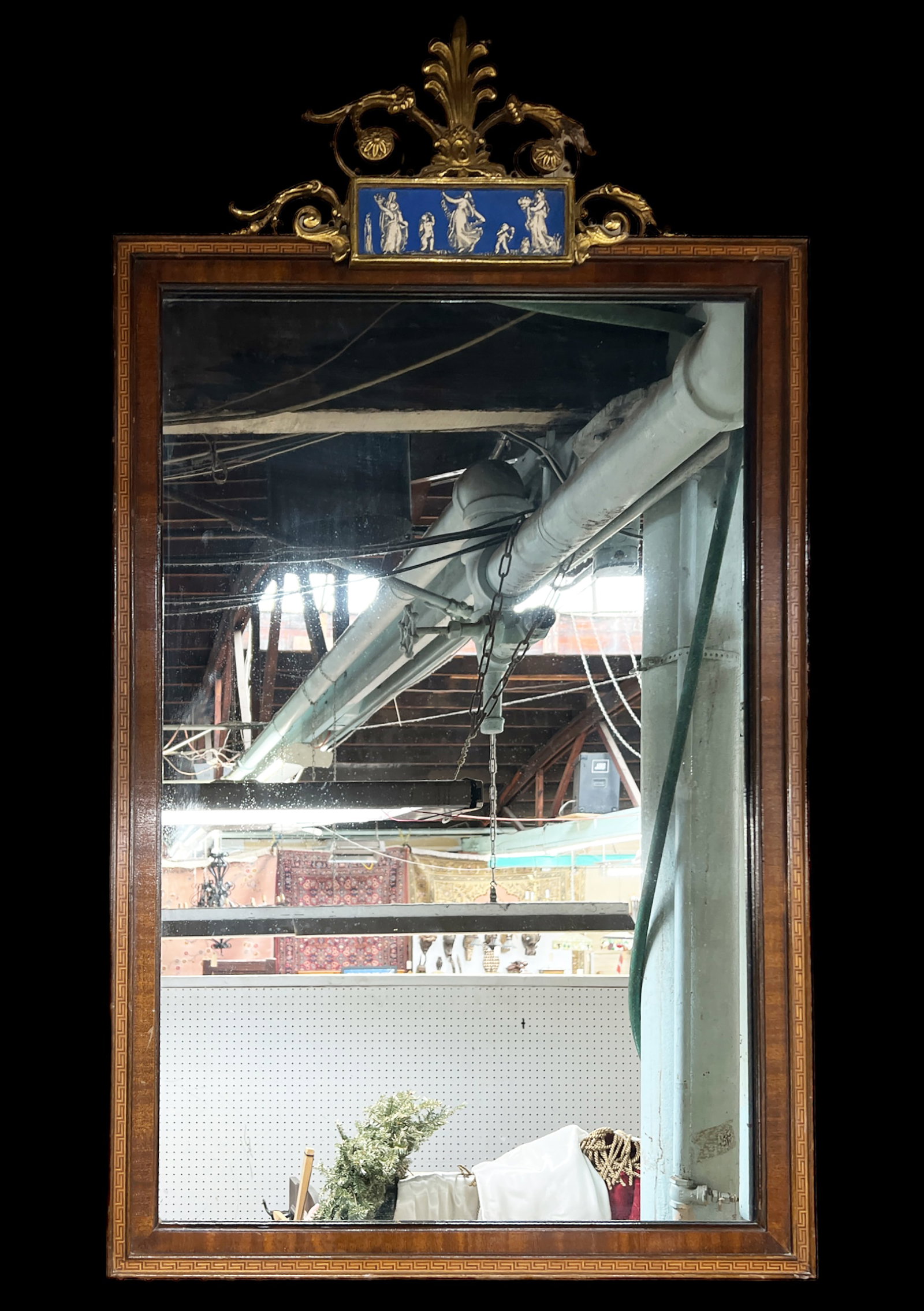 Mahogany Wall Mirror w/ Porcelain Decorations.: This mahogany wall mirror has a carved floral crest and porcelain decorations of figures. The floral crest has a broken piece and some minor scratches, but is in good overall condition. It measures 44