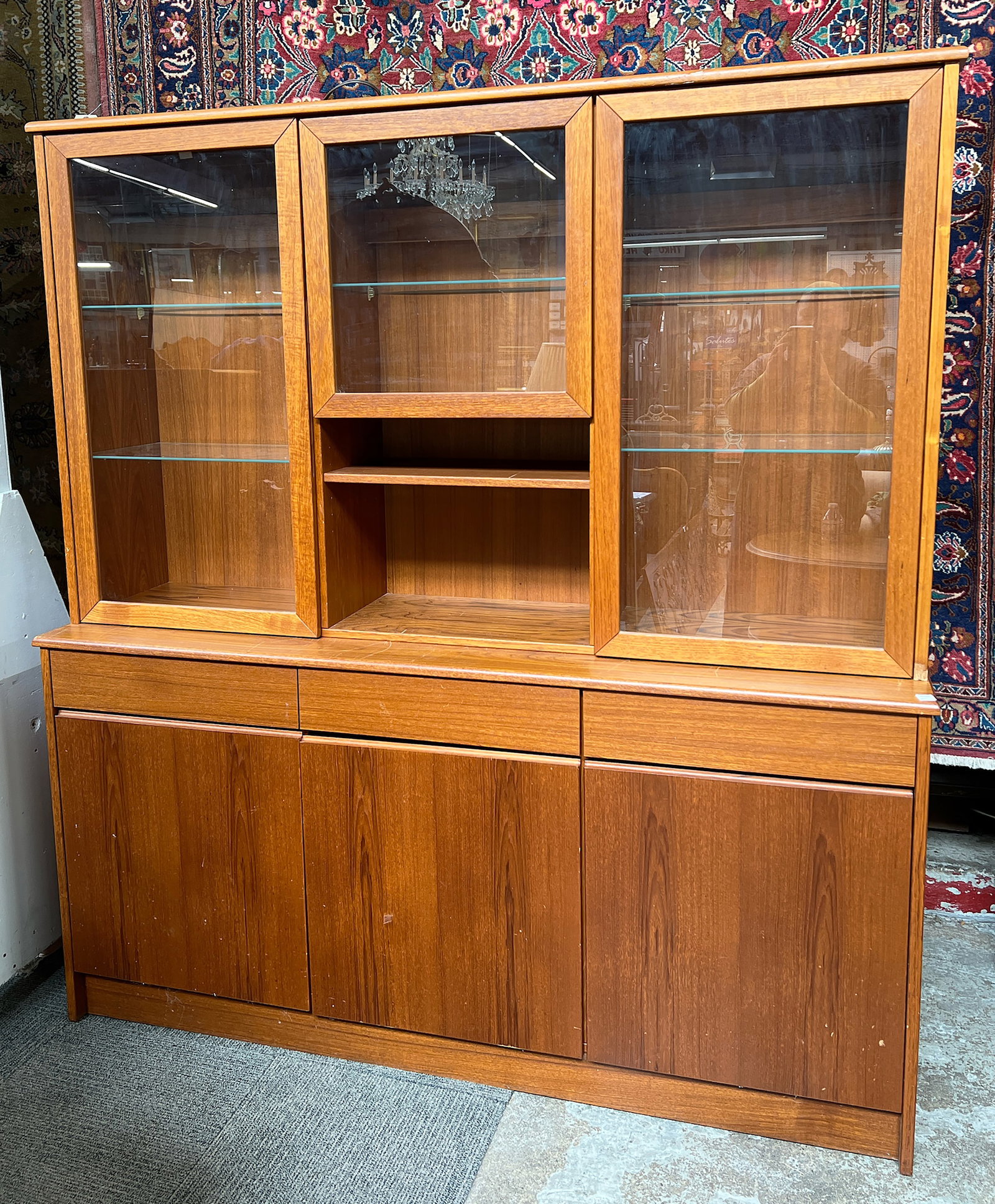 Danish Modern Teak China or Display Cabinet.: The upper section has glass shelves, and the lower cabinet has doors with three adjustable wood shelves. The rear bottom base is broken and missing a piece, and there is a piece of veneer missing alon
