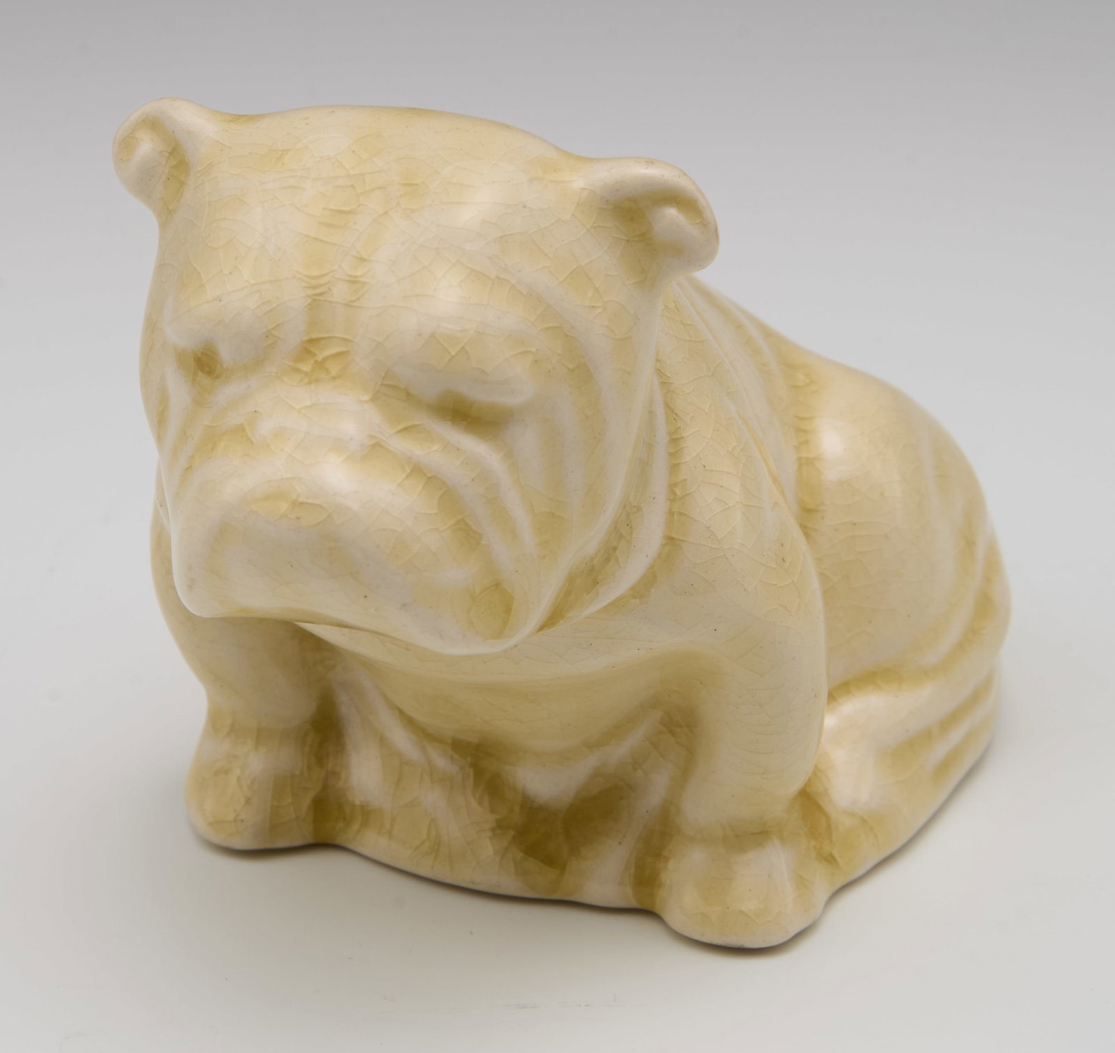 Royal Doulton Small Undecorated Bulldog w/ Flag.: This cream-colored bulldog is wearing a flag draped over its back. There is quite a lot of crazing throughout, as well as a yellowish tint to the glaze. The underside of the dog bears a Royal Doulton 