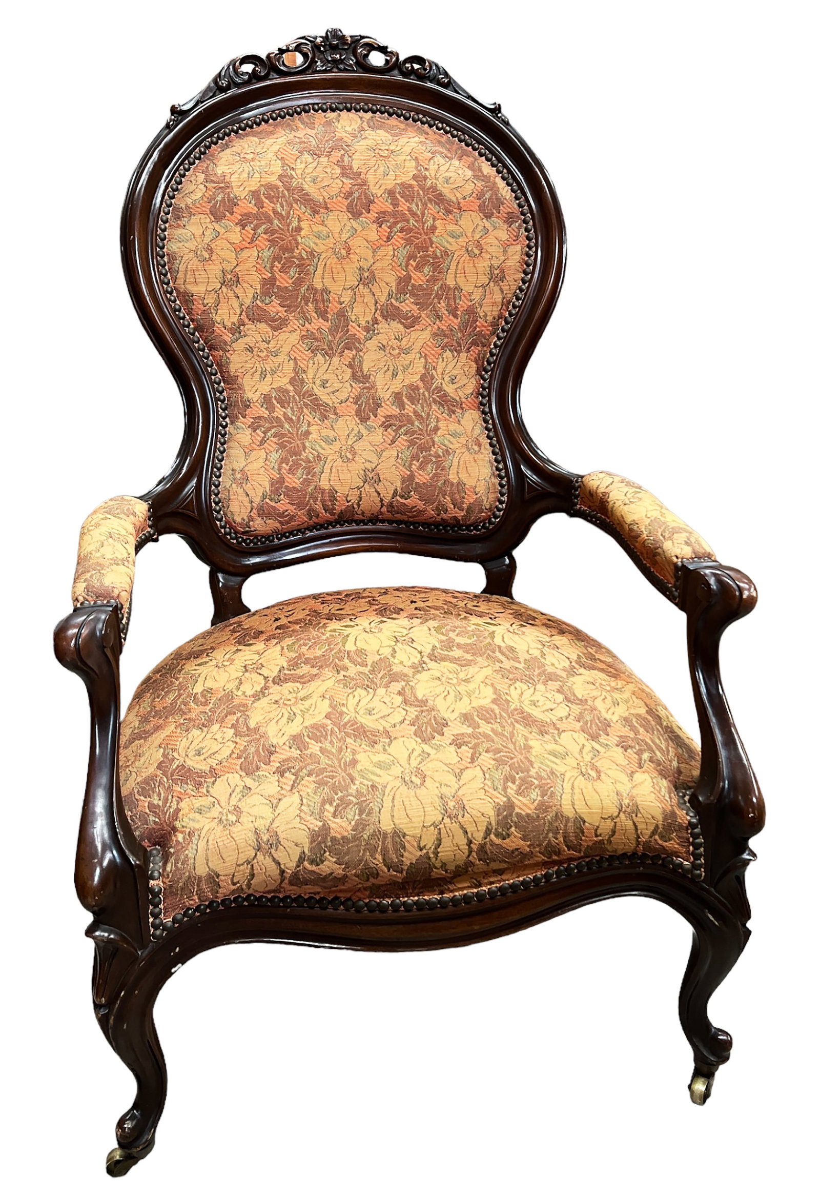 Carved Victorian Wood Armchair.: This armchair has floral upholstery, metal nail head trim, and brass casters on the front legs. The wood frame has some cracks and scratches, but overall, the chair looks to be in good condition. It m