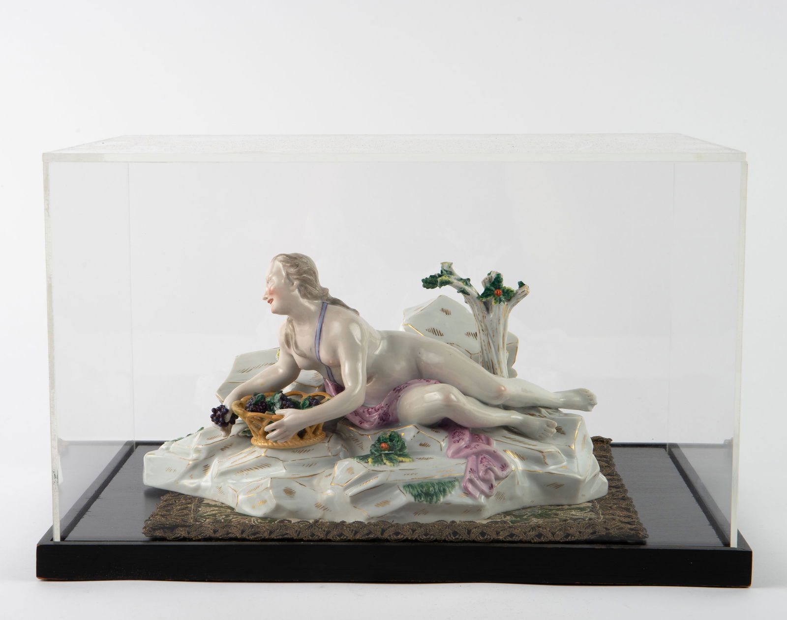 Meissen Style Porcelain Figurine - Nude w/ Basket.: The underside bears a blue crossed swords mark. The figure is quite heavy for its size. The female nude is reclining on a rock, with a basket full of grapes. There is a chip on her left foot; several