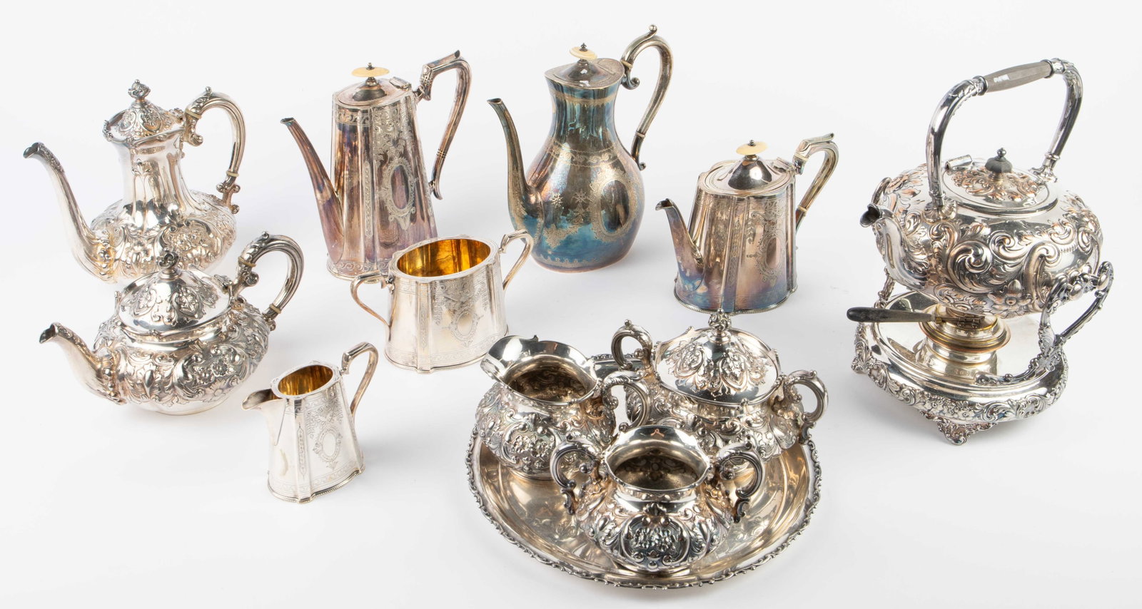Lot: 2 Antique Silverplate Tea Sets.: The chased set with bone finials is by Atkin Bros. The elaborate repousse set is by Wilcox. Also included is a round tray, which does not match either set. The largest item in the lot is the Wilcox te