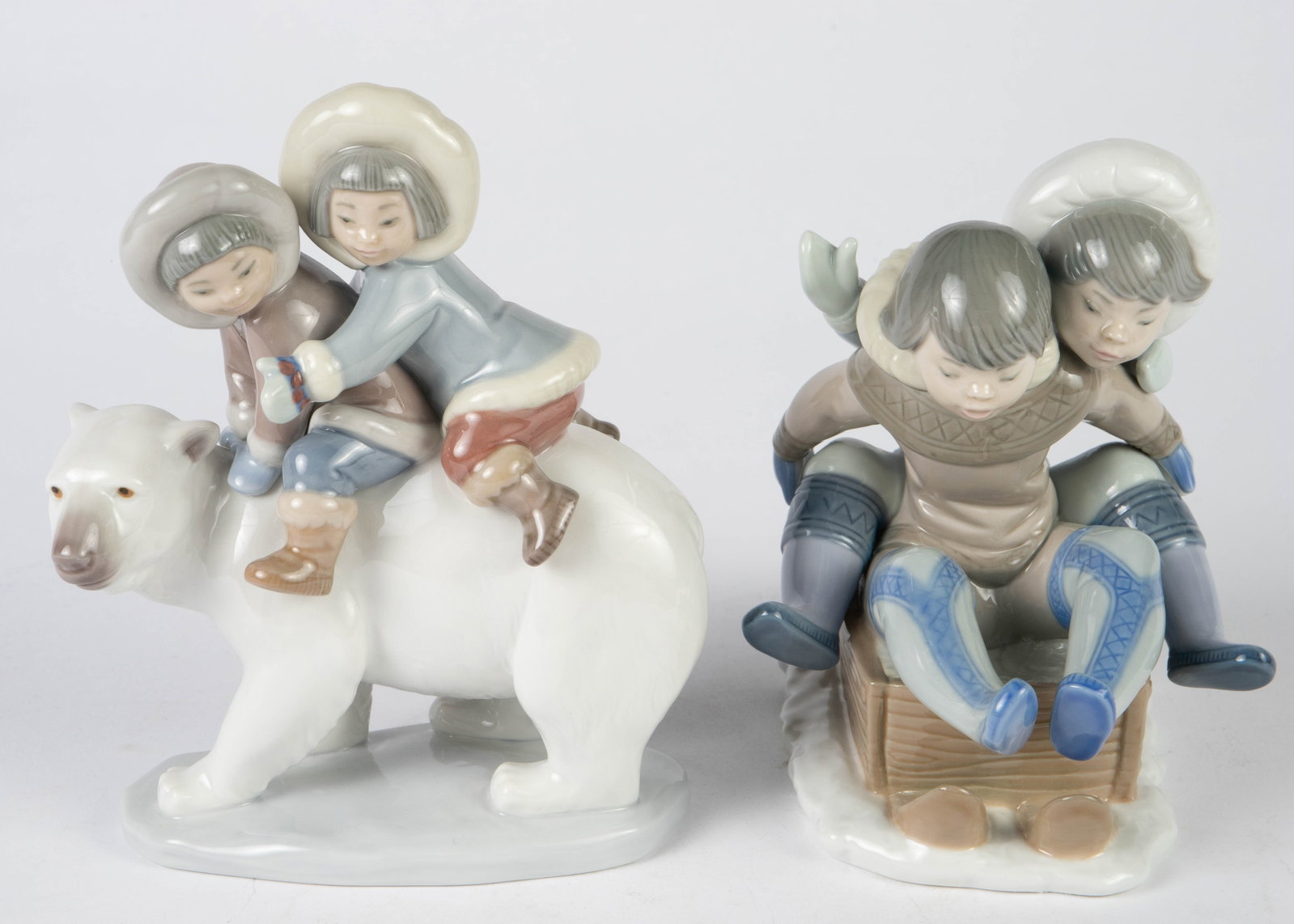 Lot: 2 Lladro Figures of Inuit Children.: One figurine depicts two children on a sled; the other figurine depicts a boy and girl riding a polar bear. Both look to be in good cosmetic condition. The larger figure measures 6 7/8" tall. In-house