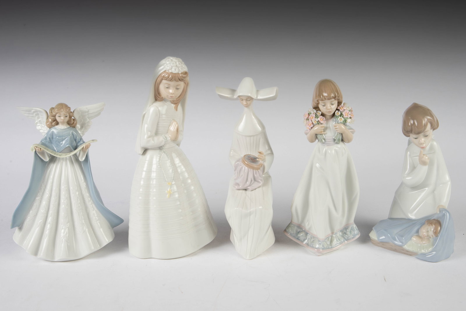 Lot of 5 Lladro & Nao Figurines.: This lot includes a young bride, a girl with flowers, a nun with an embroidery hoop, an angel holding a scroll of music, and an angel boy watching over a baby. This last item is signed by the artist. 