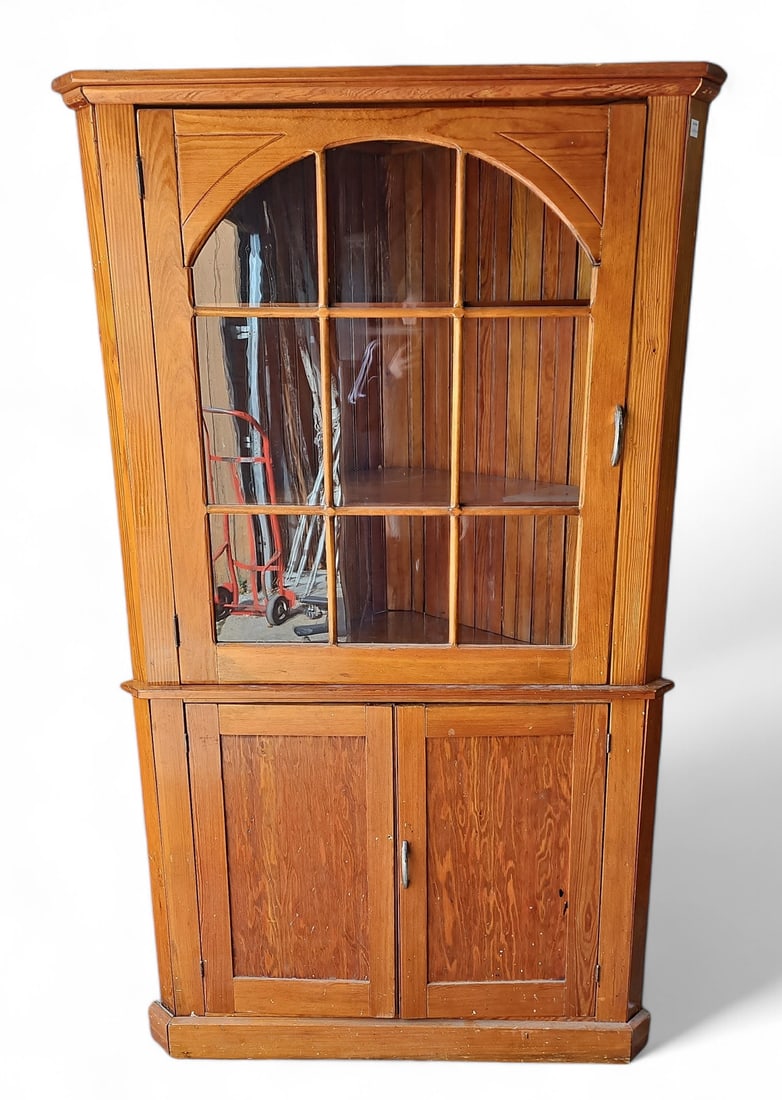 Vintage Pine Corner Cabinet.: The top half of the cabinet has a glass-front door with two fixed display shelves. The bottom half has two panelled doors that open onto a storage area with a single fixed shelf. The hardware does not