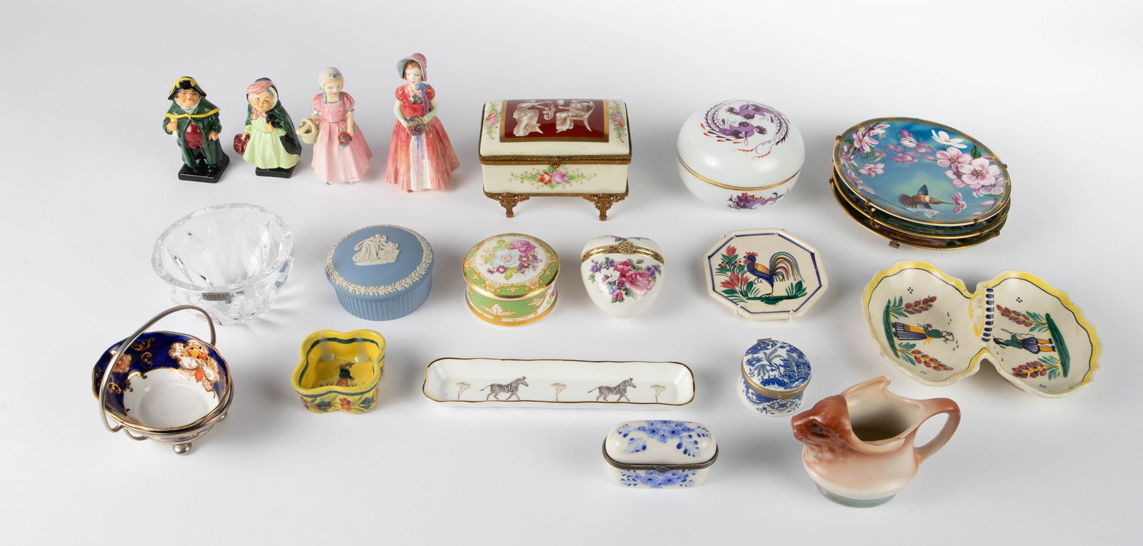 Lot: Trinket Boxes, Trinket Dishes, Figurines, etc: This lot includes four small Royal Doulton figurines, 3 Quimper dishes, a Sloane stationery pen holder, a Royal Albert bone china bowl in a metal basket, a Kosta Boda crystal bowl, a Meissen or Meisse