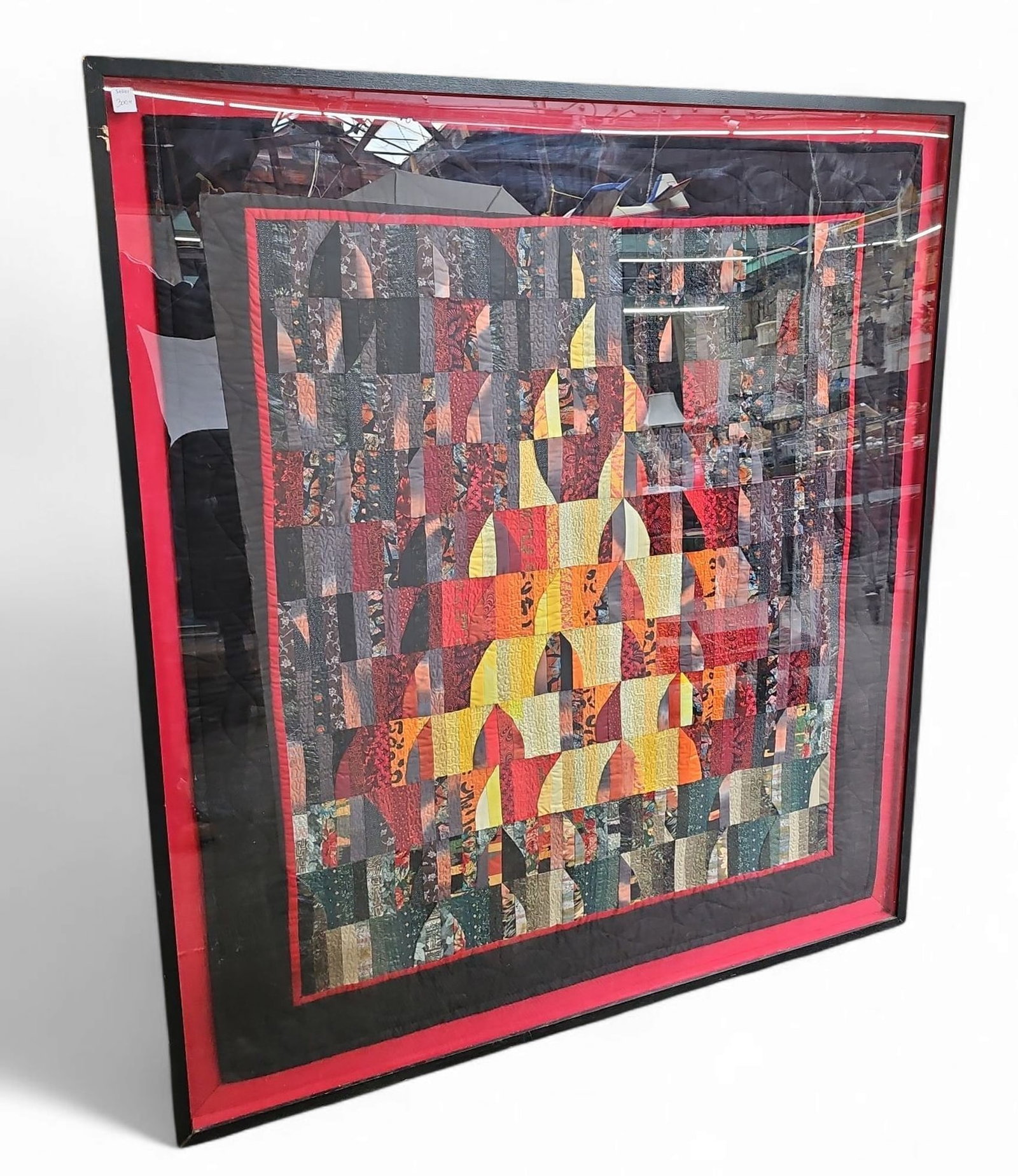 Framed Handmade Quilt in Fall Colors.: The handmade quilt is framed in a black wood and acrylic frame, and set against a red fabric background / border. The quilt measures 50" x 43 1/4". The frame measures 55" x 48". The frame has some chi