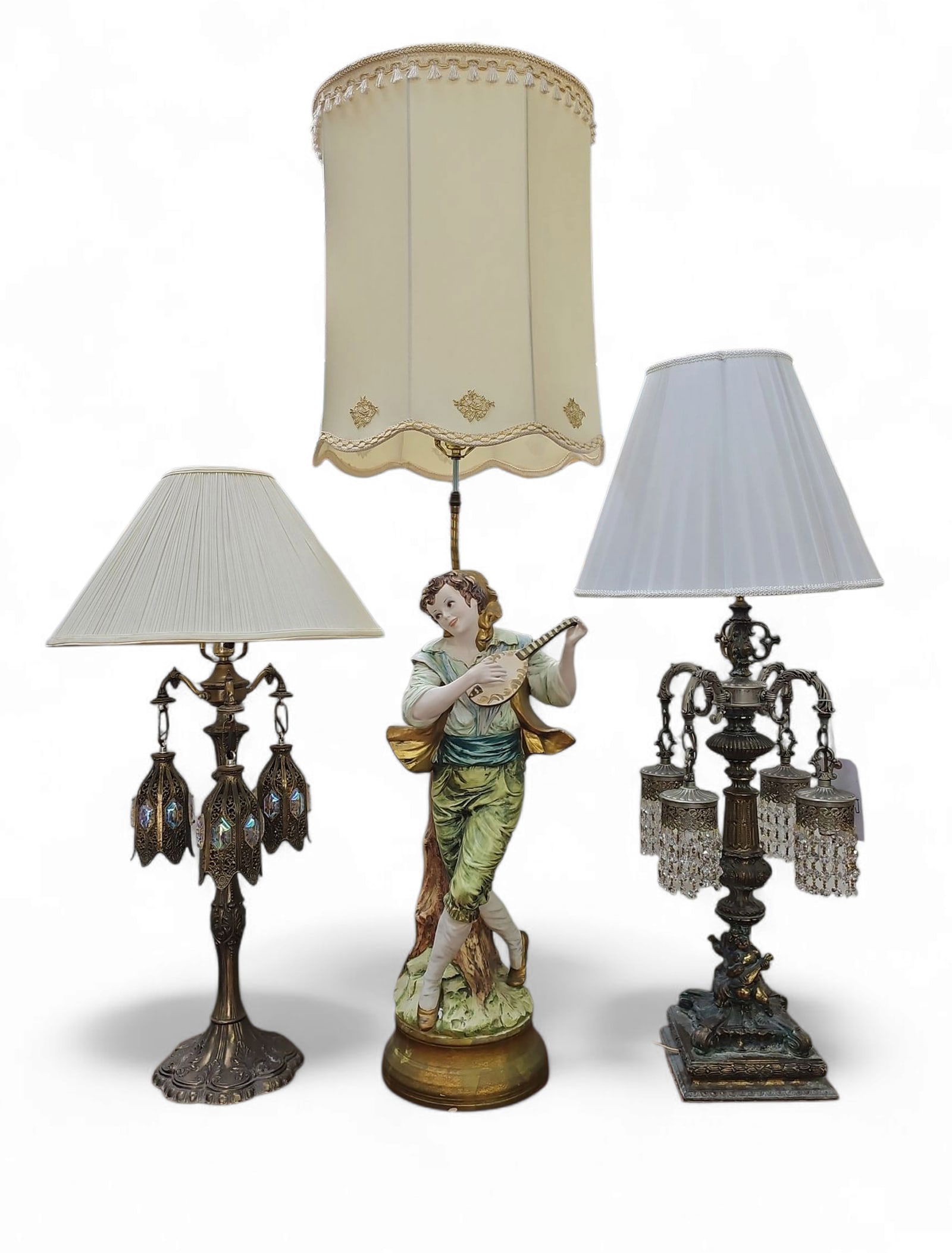 Lot of Three Ornate Lamps.: This lot consists of a Capodimonte guitarist figural lamp and two table lamps with prisms. All three are working. The Capodimonte lamp measures 55" tall, while the other lamps measure 41" tall. Third-