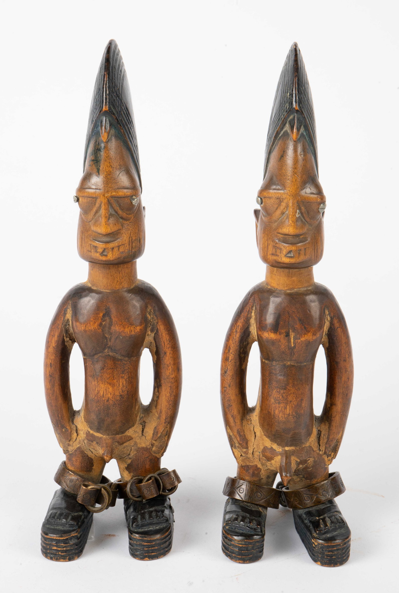 Pair of Yoruba Ibeji Twin Figures, Nigeria.: The pair of carved wooden figures depict nude men with headdresses and unlocked shackles. Each piece measures 12" x 3 1/4" x 3 1/2". There are some chips, stains and cracks on the items. Otherwise, th