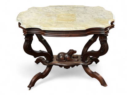 Victorian Marble Top Table with Carved Dog.: This is a nicely scalloped edge white marble top table that features a carved dog on the stretcher. The table has floral carvings, a bevelled design, and porcelain casters. The table is leaning a bit
