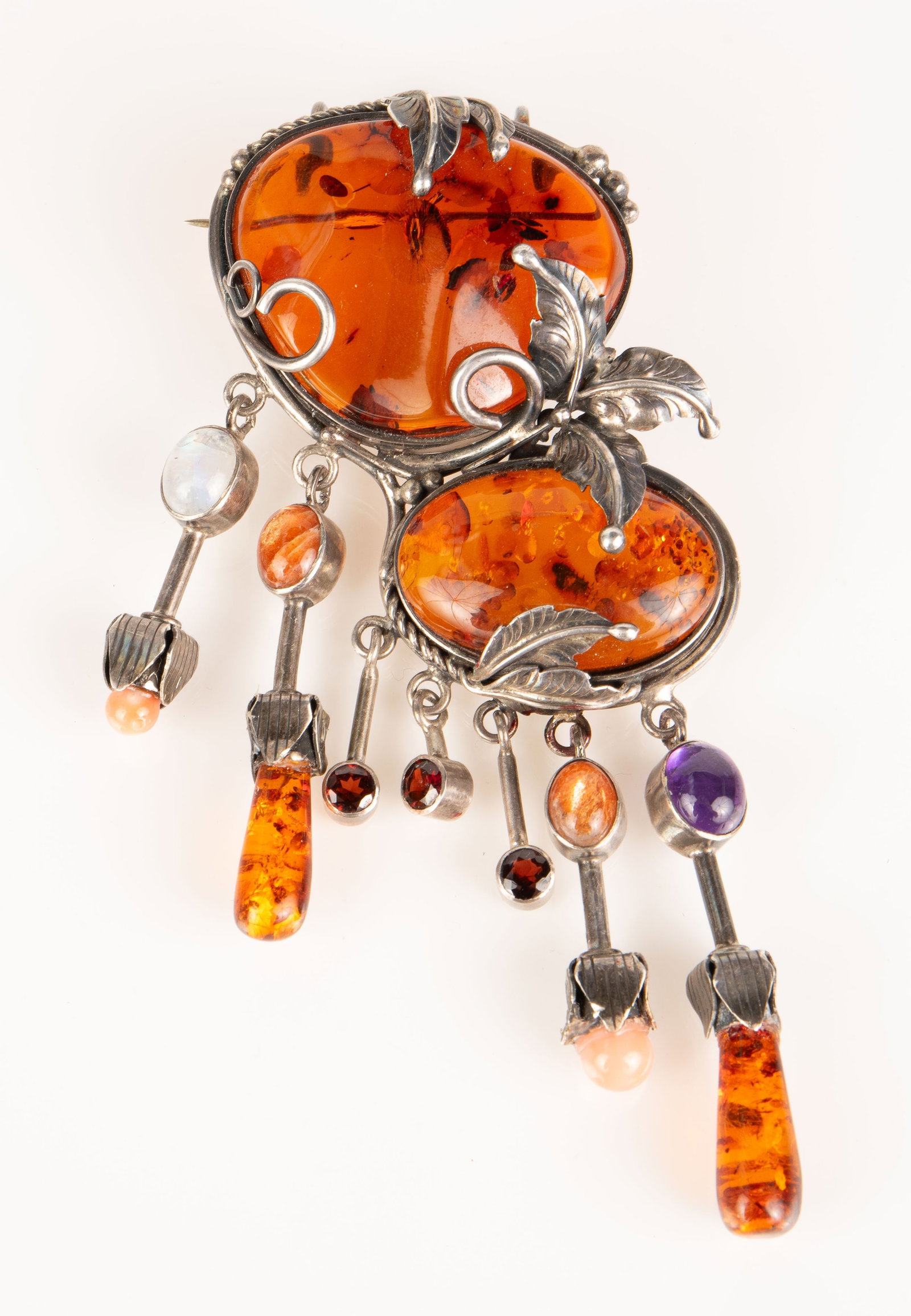 Sterling Brooch: Amber, Amethyst, Moonstone, Etc.: The pendant brooch features 2 large amber stones within a sterling silver setting with leaf decorations. The brooch also has 7 dangling pieces with amber, coral, moonstone, garnet, and amethyst stones