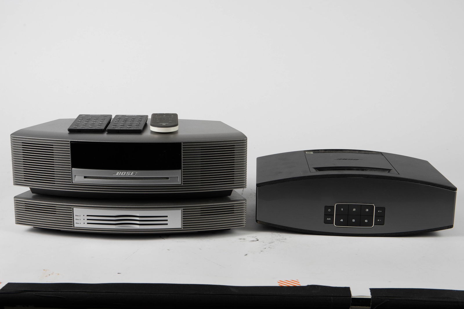 Lot of 2 Bose Radio Units - SoundTouch 20 & Wave.: The lot includes 2 Bose Radio Units. There is a black SoundTouch 20 Wi-Fi music system, model 355589, and a silver Wave Radio music system with a charger accessory that is placed below the speaker. Th