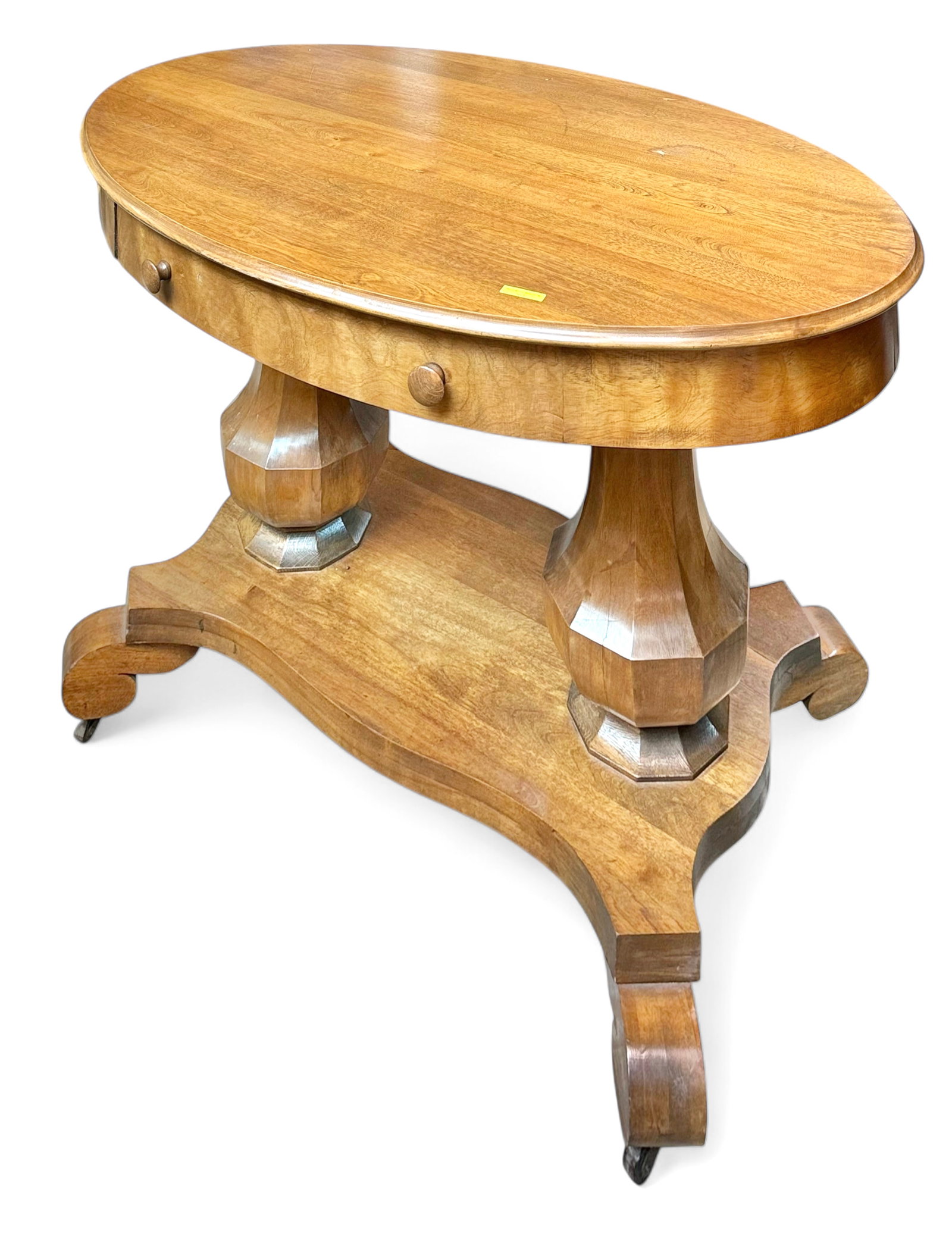 Empire Oval Console Table.: This light wood table has a double pedestal design, and sits on casters. It has one central drawer with wood pulls. There are some scratches and stains on the wood, and the bottom of the drawer is cra