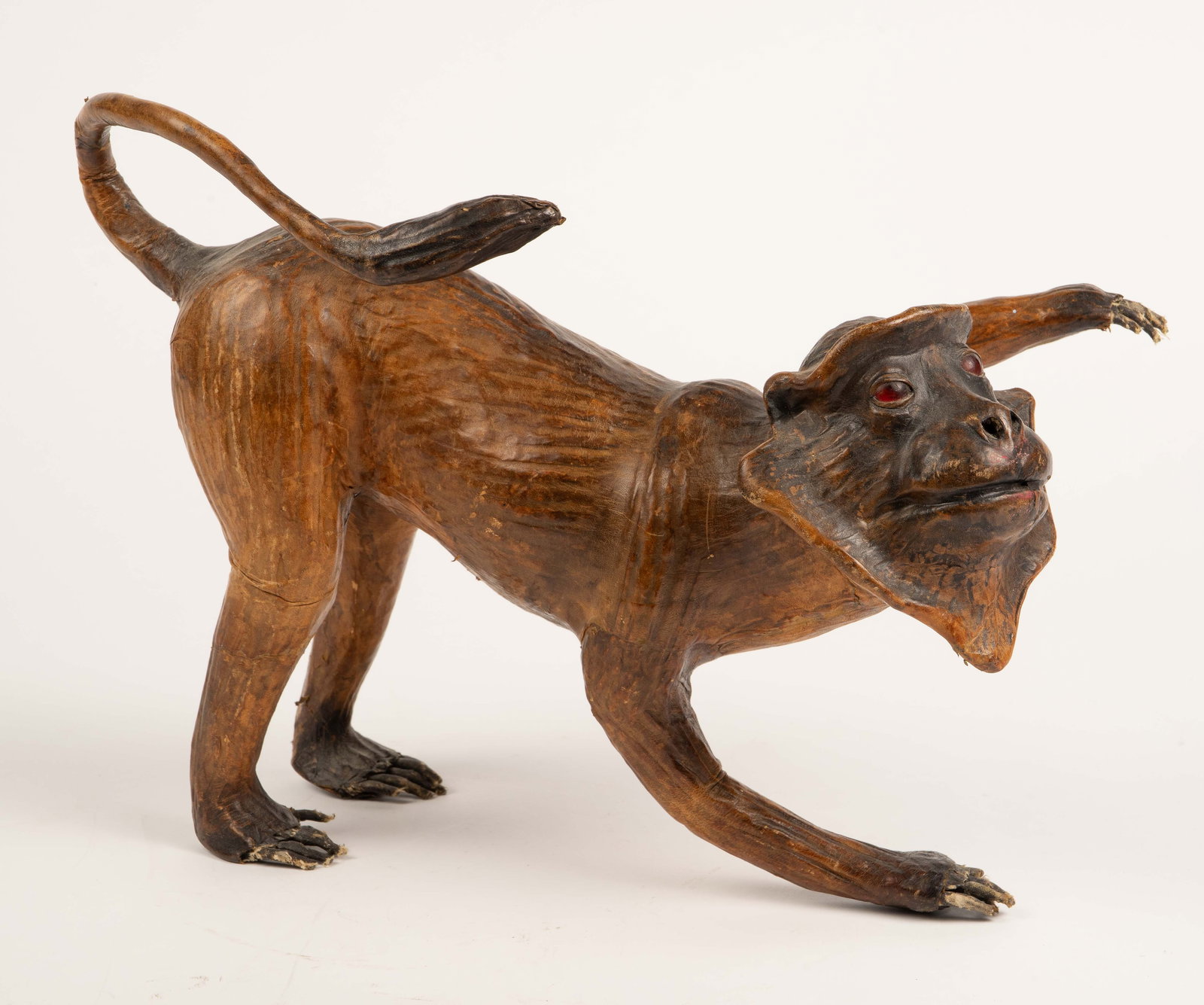 Antique Leather Wrapped Macaque Monkey Sculpture.: The sculpture is a composition made of wire, fabric, paper mache, and leather. It features a macaque monkey with red glass eyes. It stands alone on three feet. It measures 10 1/2" x 14 1/2" x 8". The
