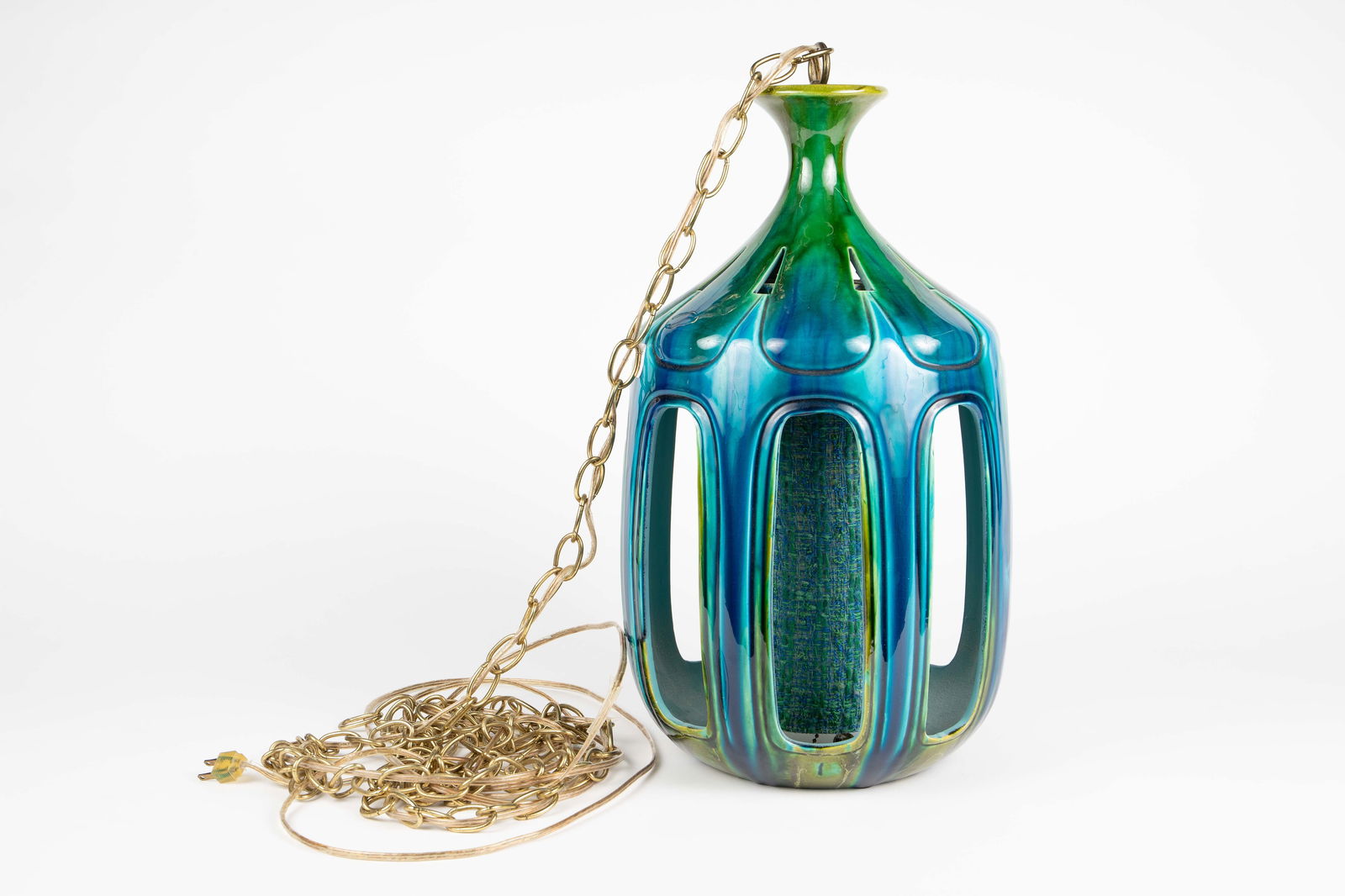 Attributed to Honi Chilo Ceramic Pendant Light.: This 1970's pendant light features a pierced ceramic exterior in teal and green glaze, and a tweed fabric wrapped cylinder at the center. The piece comes with a brass chain. It measures 20 1/2" x 12".