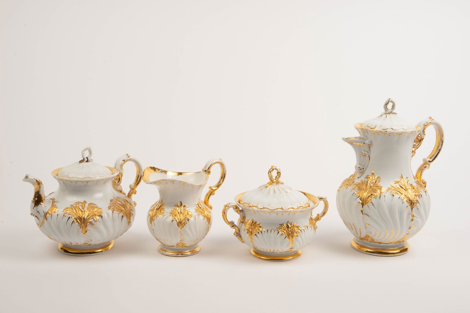 Meissen Cattail Gilded Porcelain Tea / Coffee Set.: The set contains 4 pieces of the same design. There is a tea pot, a coffee pot, a double handled sugar dish, and a small milk or creamer jug. The pieces have a cattail and oyster shell design with orn