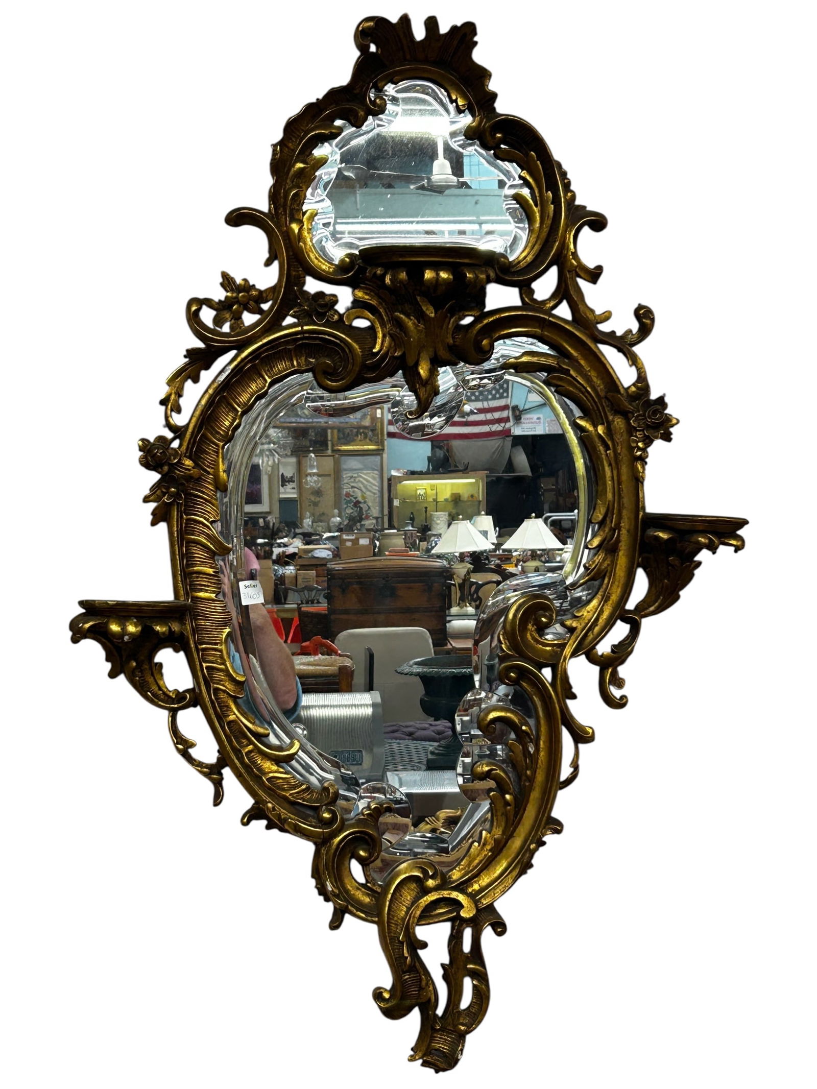 Hollywood Regency or French Style Wall Mirror.: This ornate gilt mirror has two bevelled mirror panels and three candle stands or small shelves. The frame is decorated with carvings of flowers and acanthus leaves. There are some small chips here an