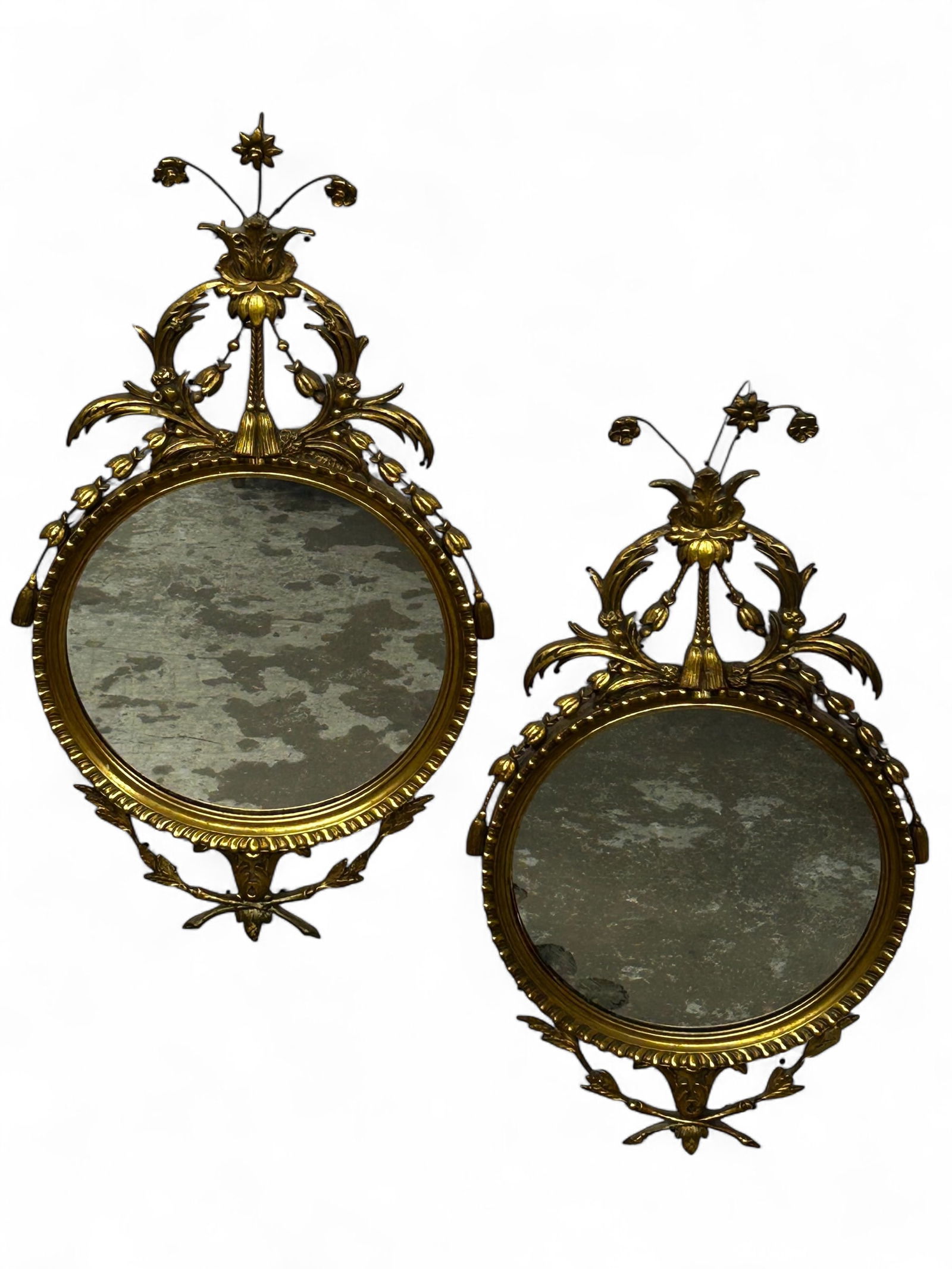 Pair of Vintage Giltwood Wall Mirrors.: These circular mirrors each have elaborate floral crests and carvings of leaves. They are in good condition overall. A couple of the leaf carvings are damaged on one of the mirrors. The other mirror s