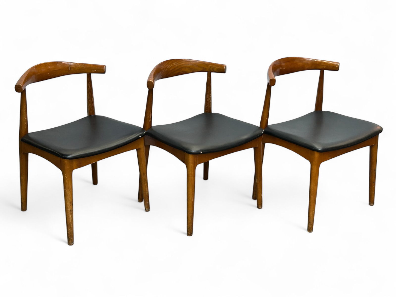 Set of 3 Mid Century Hans Wegner Style Chairs.: The lot consists of 3 Mid Century Modern chairs in the style of Hans Wegner. They have black vinyl seats and tapered legs. Each measures 29 1/4" x 20" x 20". There are some scuffs and stains on the wo