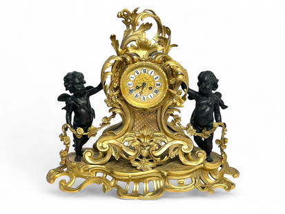 French Gilded Table Clock w/ Cherub Figures.: The large rococo style keywind mantel clock has a beveled crystal, porcelain number plaques, pierced scroll, fan, and flower designs, and black cherub figures on either side. The gilded metal is