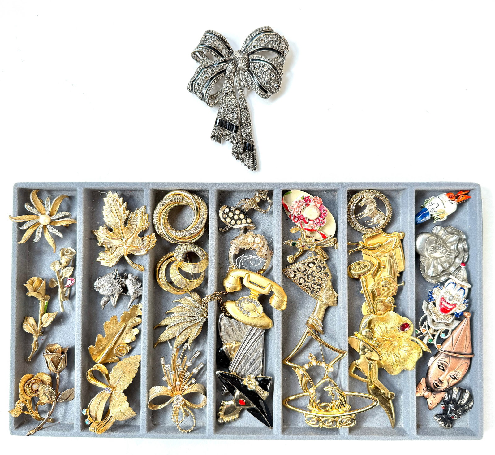 Lot of Vintage Costume Brooches, inc. HAR.: The lot contains 32 vintage brooches. They are in the designs of bows, leaves, flowers, portraits, women, a god, a donkey, a hat, clowns, a car, and abstract shapes. They are mostly gold toned metals 