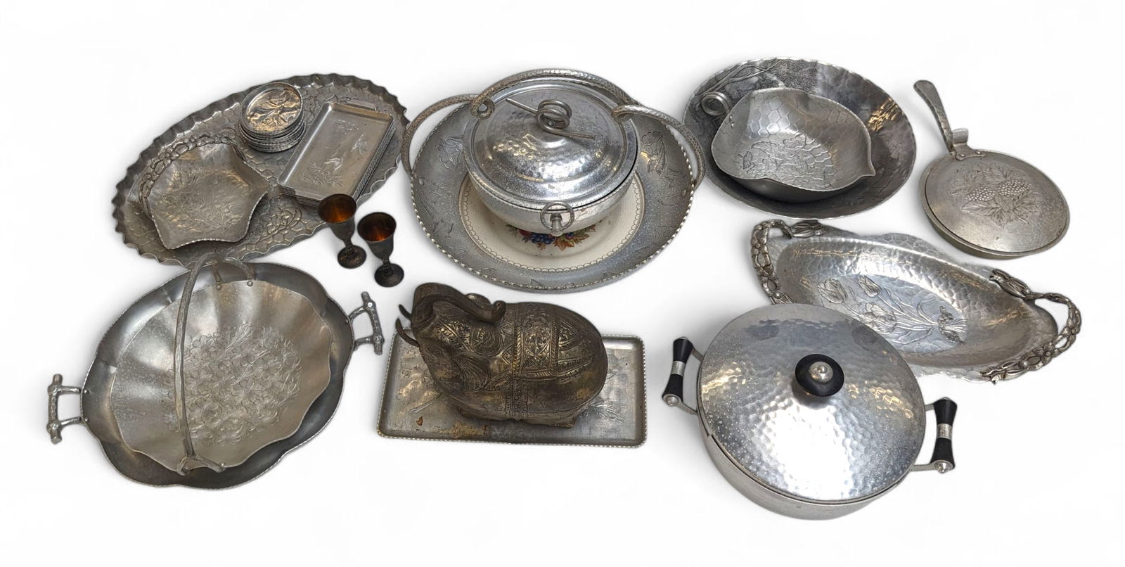 Lot of Wrought and Forged Aluminum Items.: The lot contains 28 items, mostly aluminumware. There are trays, coasters, bowls, pots, a pan, and more. The lot also includes a pair of silver plated cordials by Roma S.L., Madrid, and an Asian hamme